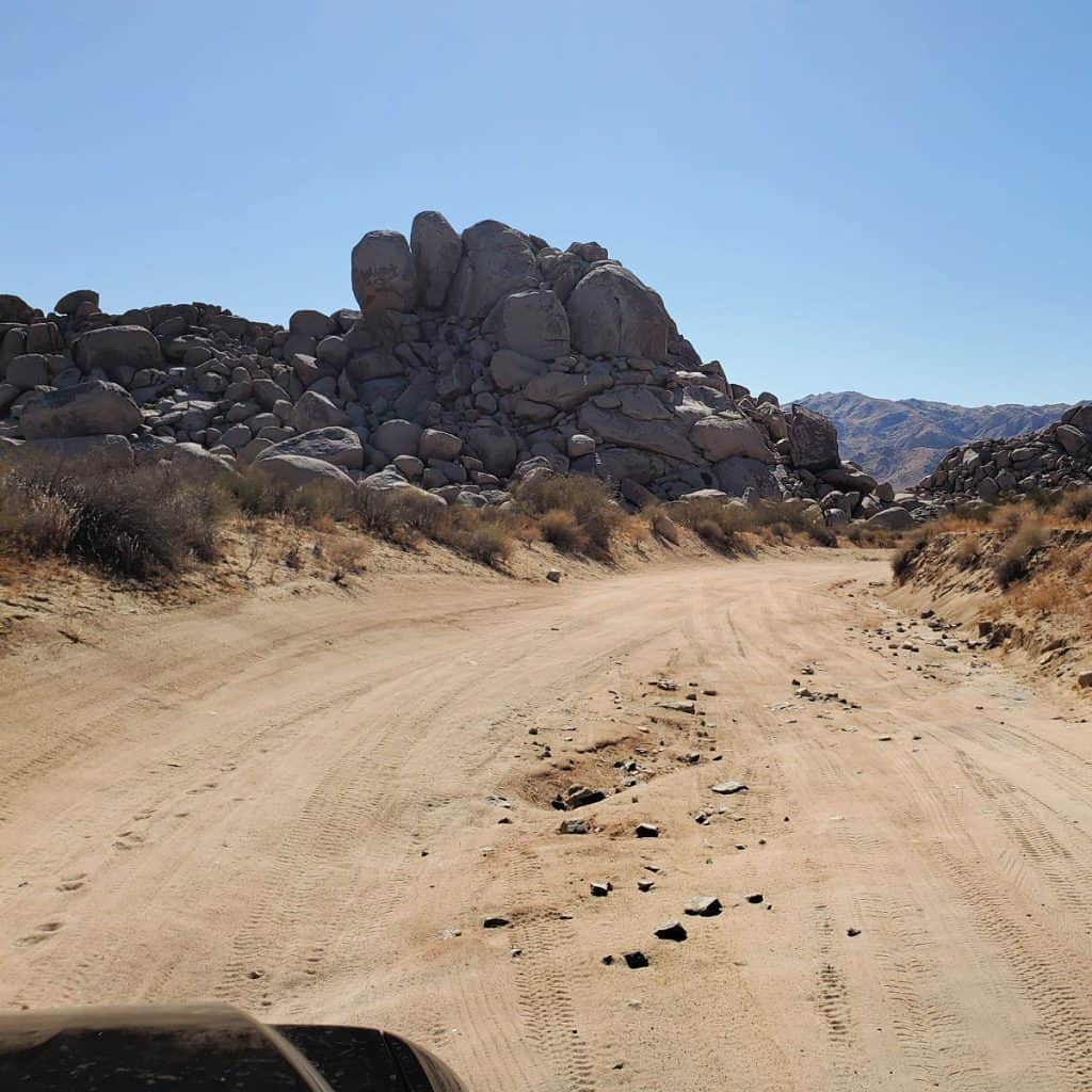 heavily rutted dirt road with large rock formations and blue skies on the Geology Tour Road in Joshua Tree National Park