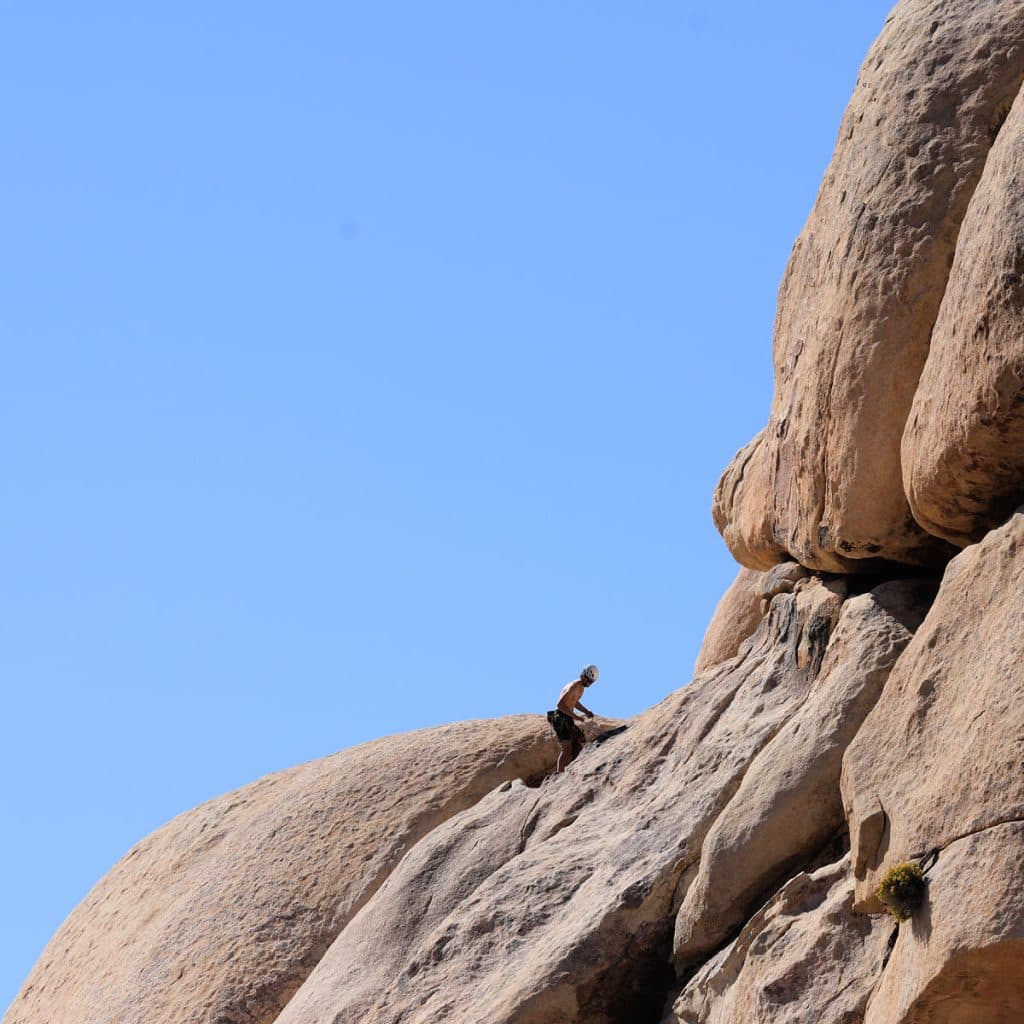 person rock climbing with ropes on large boulder at Joshua Tree National Park