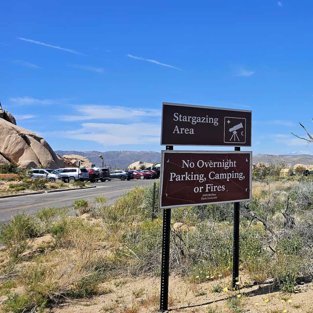 Sign pointing to the Stargazing Area in Joshua Tree National Park with a parking lot with several cars in the background.